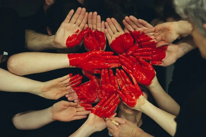 Red-painted hands united in an artistic circle symbolizing HIV solidarity and dismantling stigma