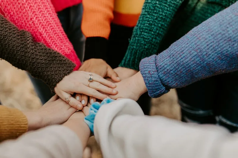 Hands stacked together in warm knitwear representing UK peer support groups and community charities